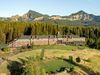 A mountain lodge surrounded by forest with rugged peaks rising behind.