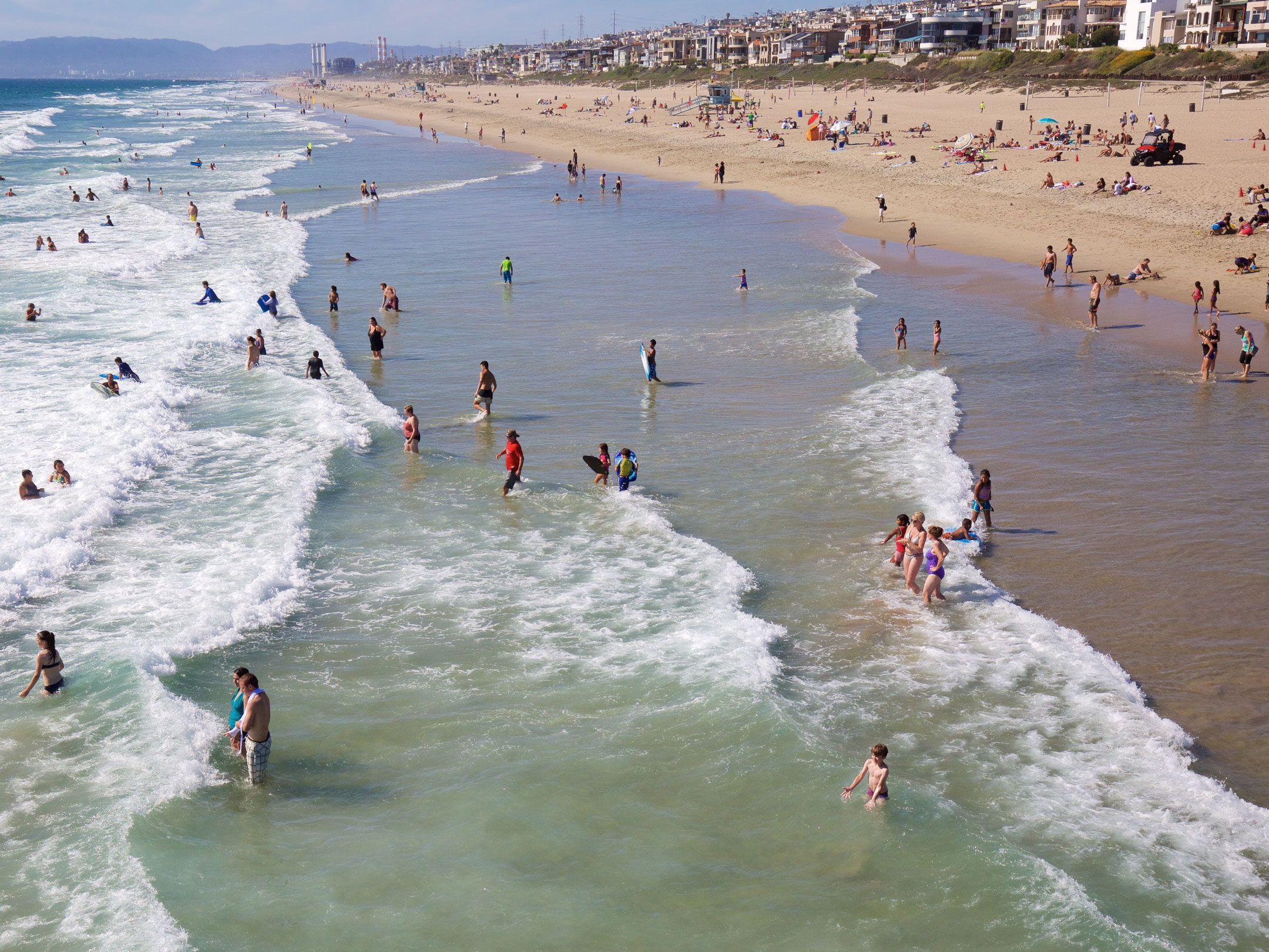 Aerial view of people swimming and walking in the water with the beach in the background.