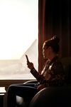 Person sits at a window looking at their phone.