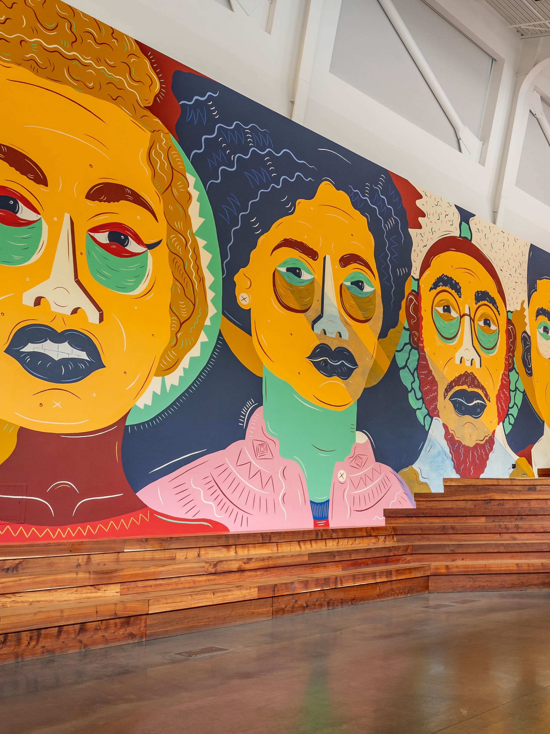 Colorful mural of stylized faces displayed on a large interior gallery wall.