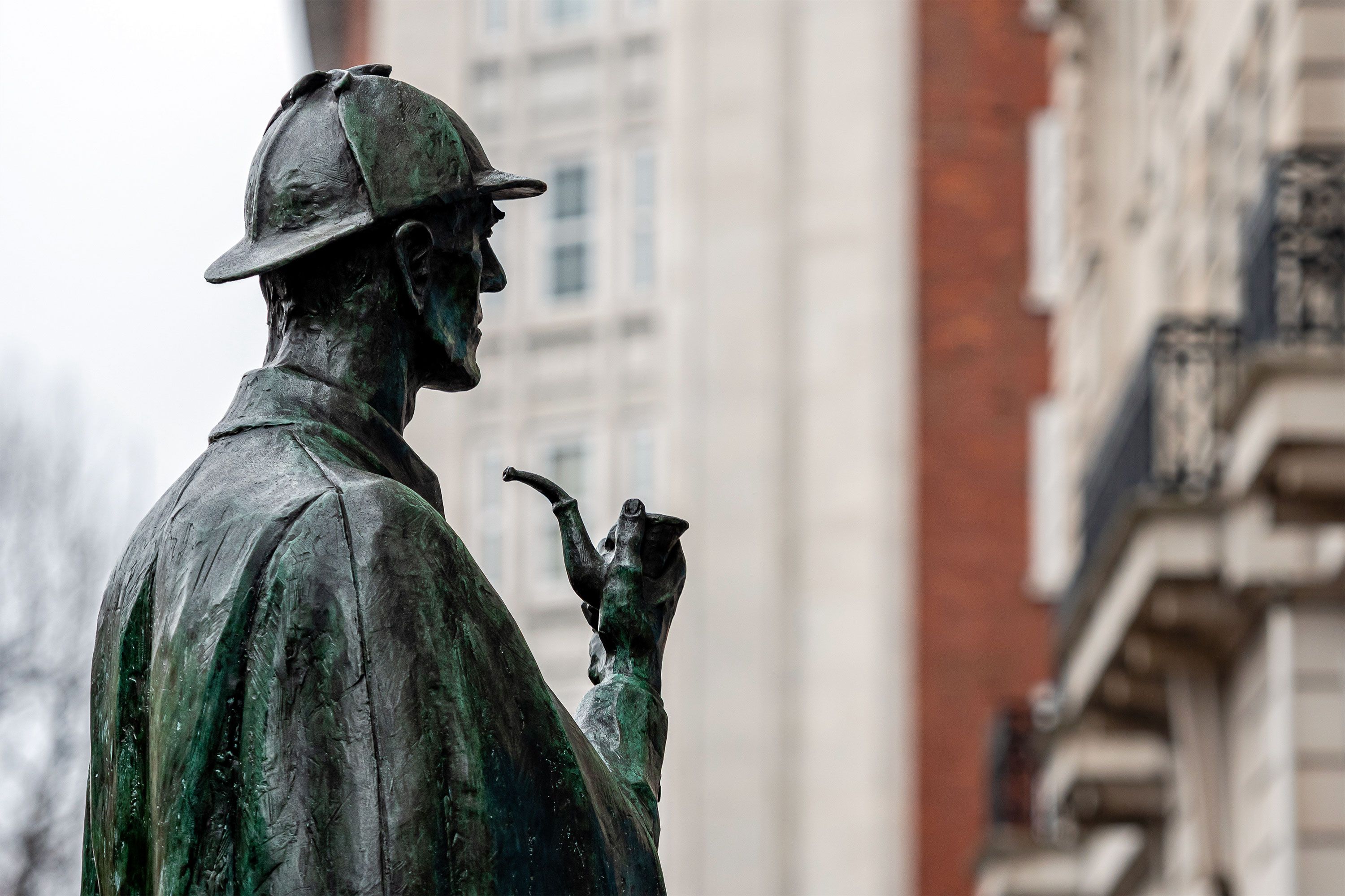 Bronze statue of a detective holding a pipe, seen in profile outdoors.