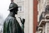 Bronze statue of a detective holding a pipe, seen in profile outdoors.
