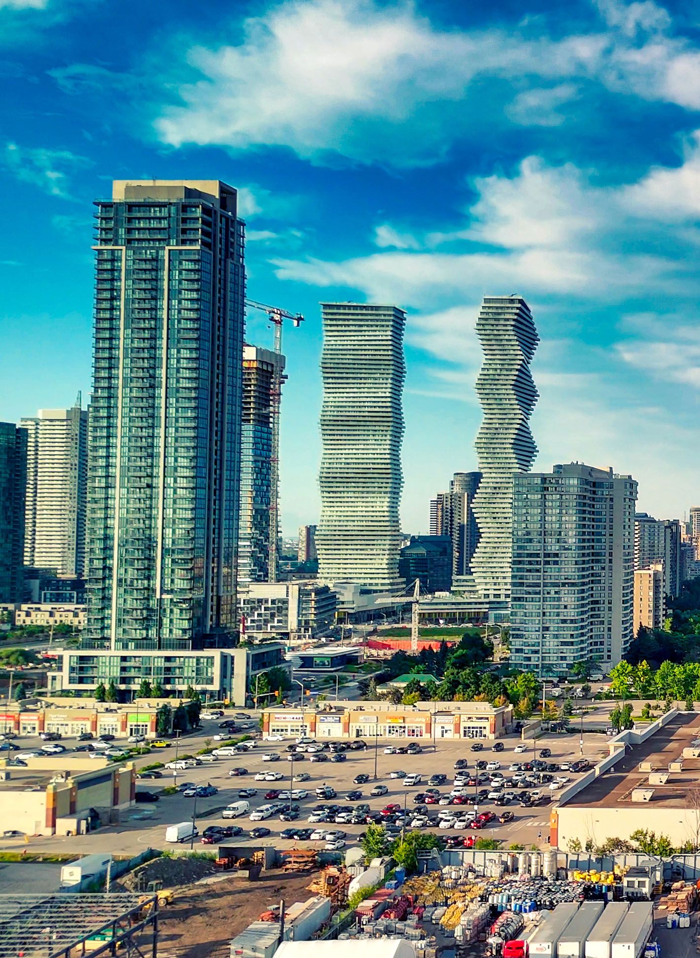 Tall buildings, with some wavy architectural details, against blue skies above and street vendors below.