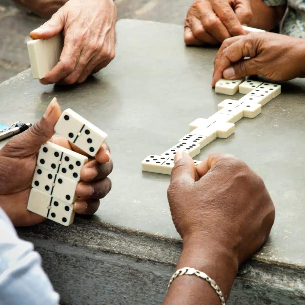 Close-up of a game of dominoes with three players on a stone outdoor table