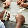 Close-up of a game of dominoes with three players on a stone outdoor table