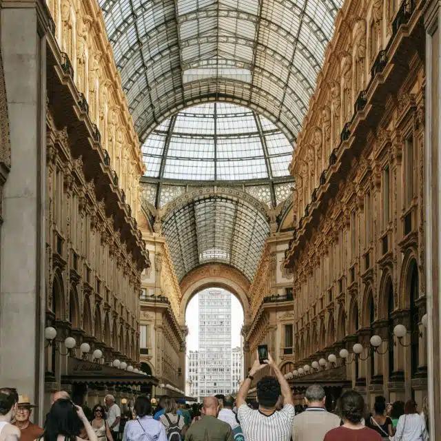 A visitor raises their phone above the crowds to photograph the Galleria Vittorio Emanuele II, Milan