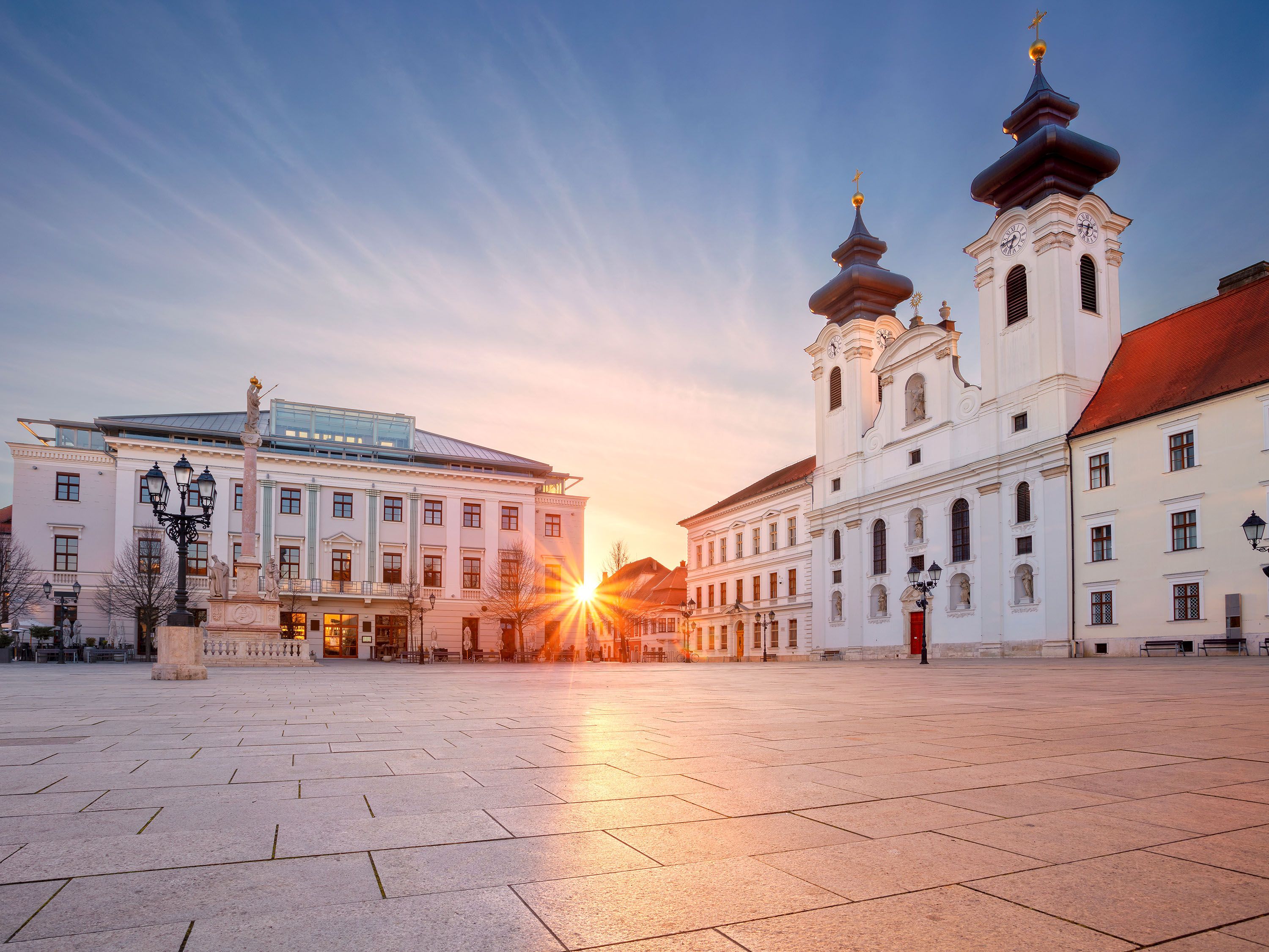 Sun sets on a town square surrounded by white buildings.
