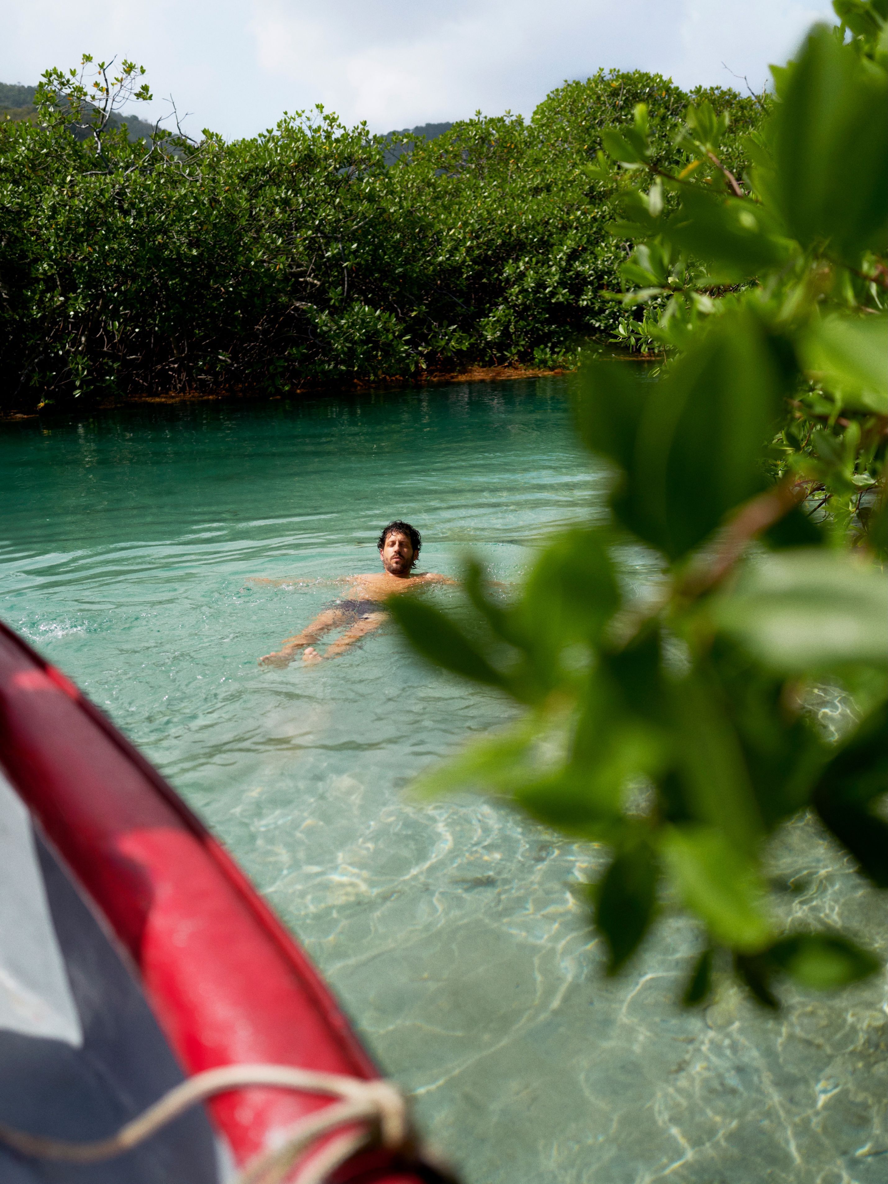A man floats on his back in the blue waters of the Tunnel of Love, a mangrove sea channel near to Isla Mamey, Panama