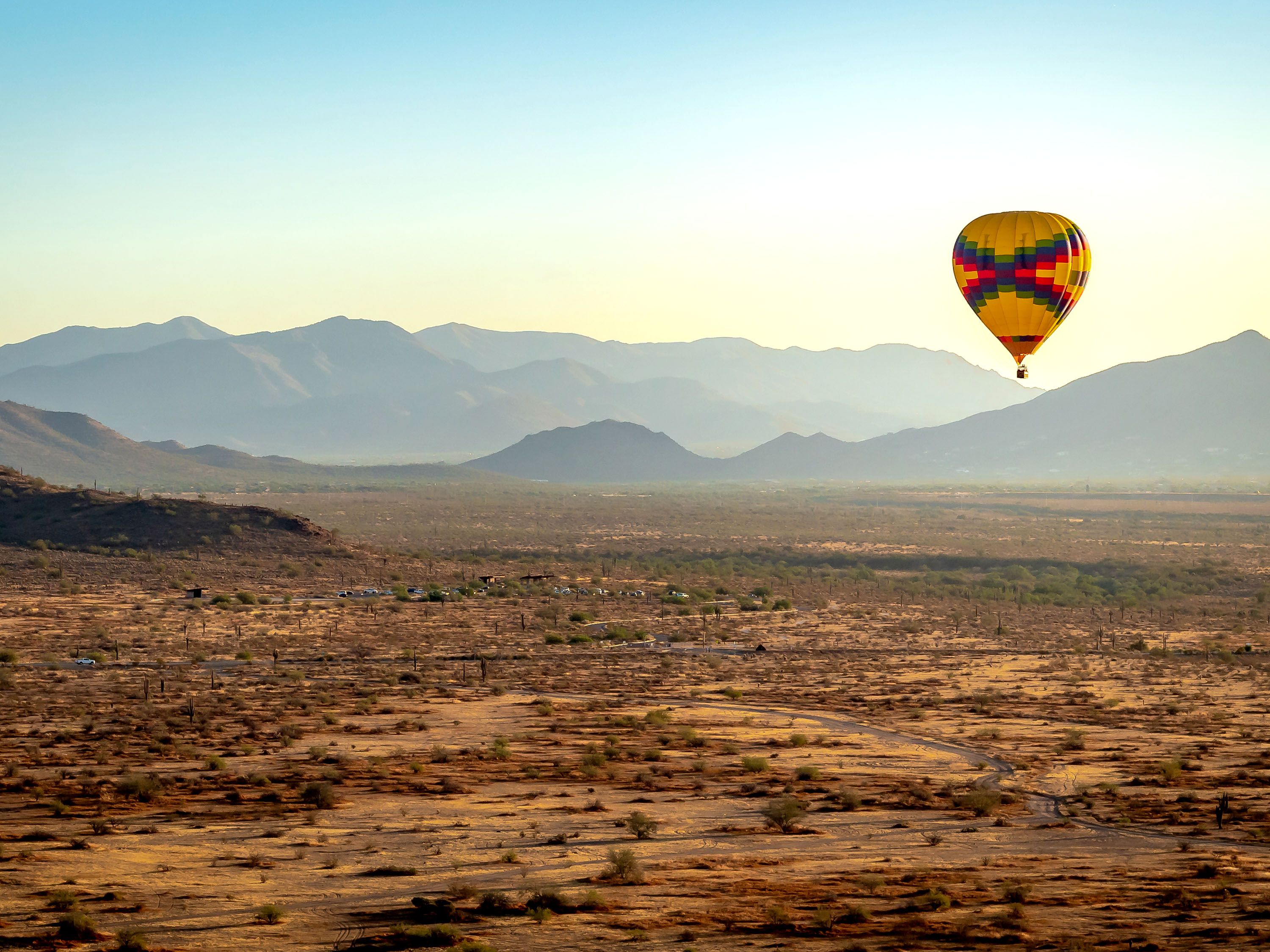 Hot air balloon over desert with mountain range.