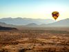 Hot air balloon over desert with mountain range.