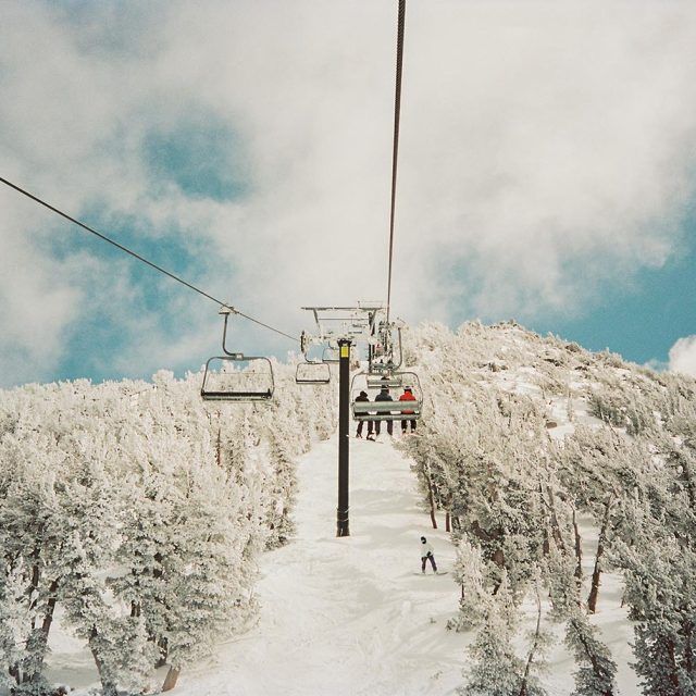 A ski chairlift ascends a snowy mountain covered with trees