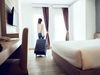 Back of woman dragging suitcase into crisp hotel room.