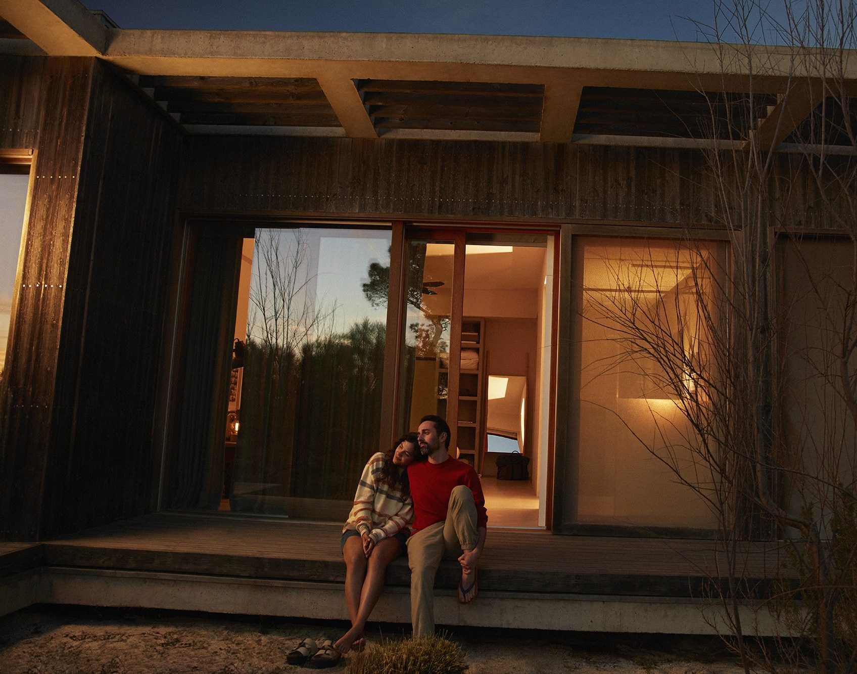 A couple sits on the steps of a home as sun sets