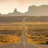 A long straight road cuts through the middle of a desert landscape with a mountain range in the distance