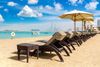 Rows of empty sunbeds and straw parasols set on a sandy Abu Dhabi shoreline, with the turquoise gulf water and a clear sky in the background.