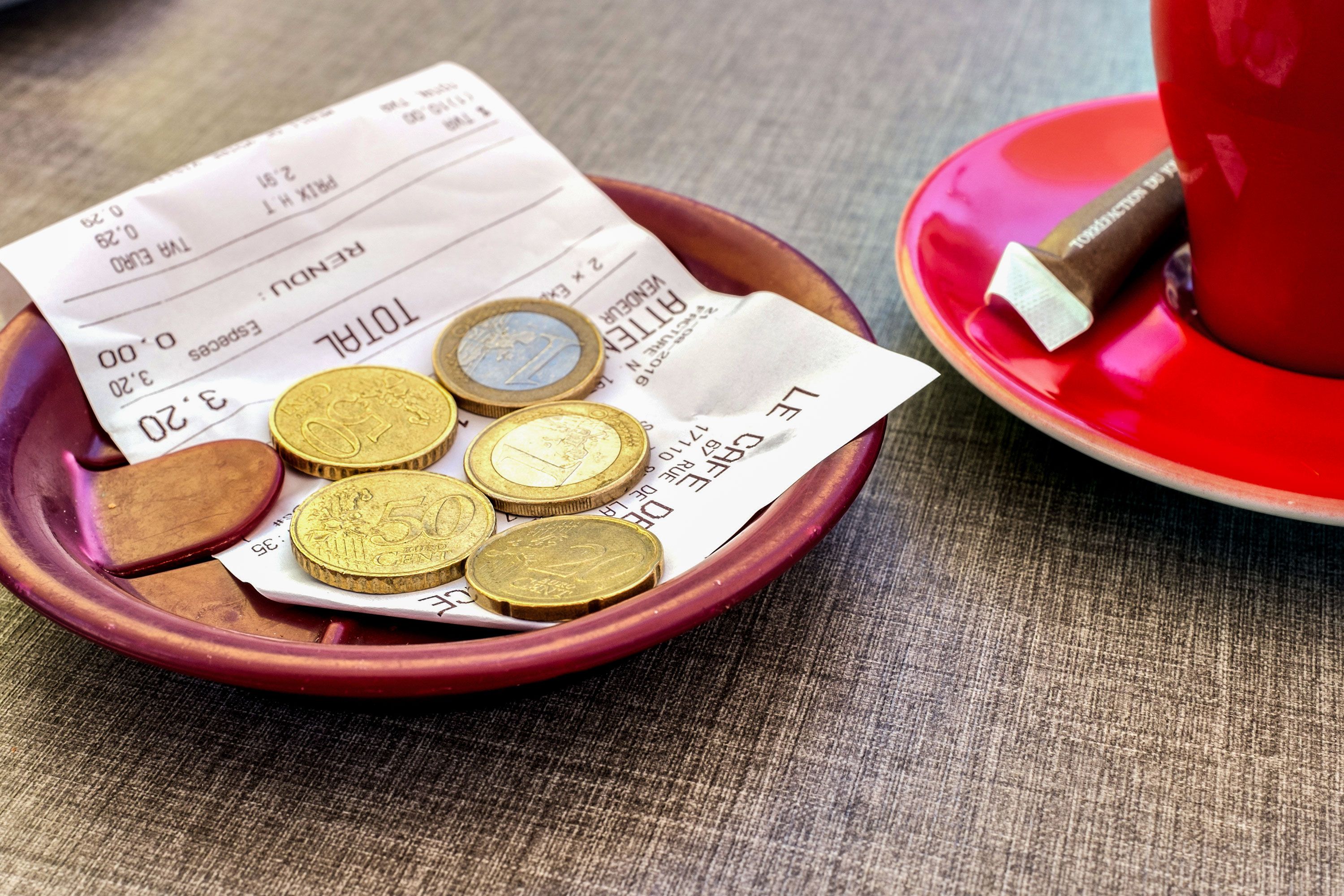 Euro notes left as a tip rest on a receipt atop a plate on a table