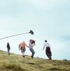 With a camera crew and microphone boom in front of him, actor Leo Woodall climbs Arthur's Seat in Edinburgh, in a behind-the-scenes shot from One Day (photo courtesy of Netflix)