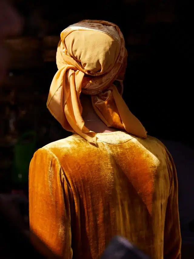 A painterly image of a woman from behind, wearing mustard velvet and a matching scarf knotted around her head