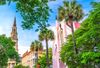 View of colorful buildings including a steeple along with palm trees.