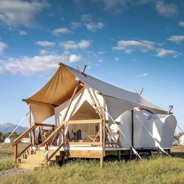 A wood and canvas glamping set-up at Under Canvas, Yellowstone, with a bright blue sky above and grass below