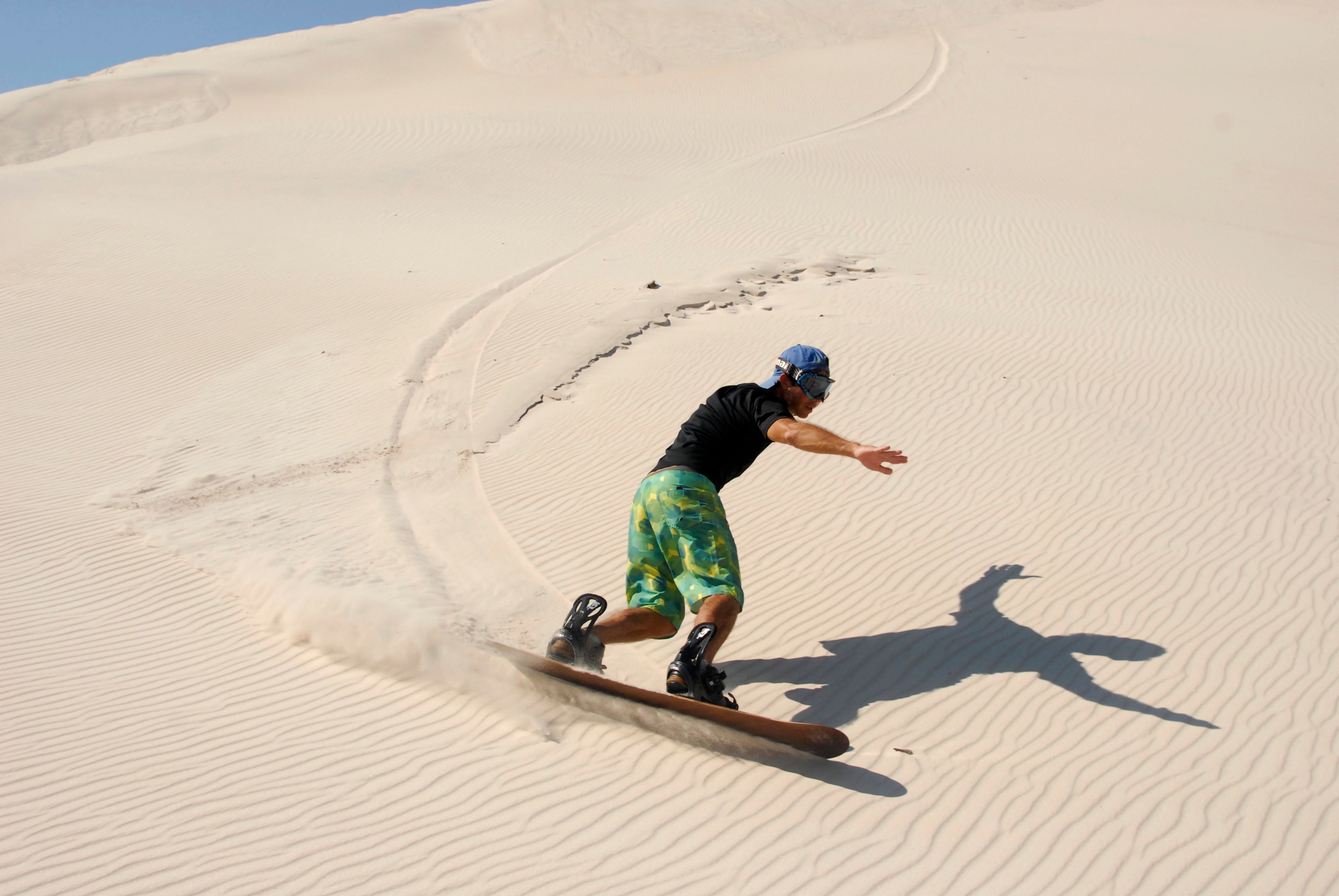 Person sandboarding down a sunlit dune.