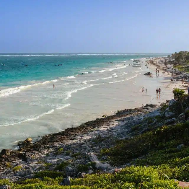 Turquoise waters meet white sands leading to rocky cliffsides along the coast in Tulum, Mexico