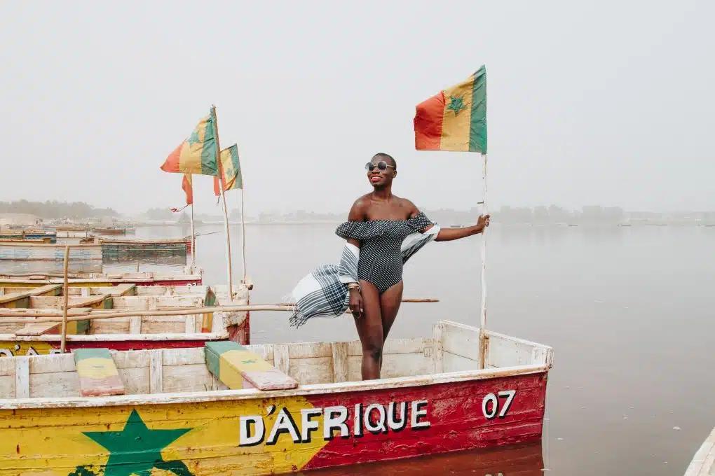 Jessica Nabongo stands aboard a red, yellow and green boat on on Lac Rose in Senegal