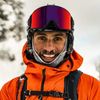Pro skier and accessibility activist Vasu Sojitra wearing reflective ski goggles and an orange ski jacket