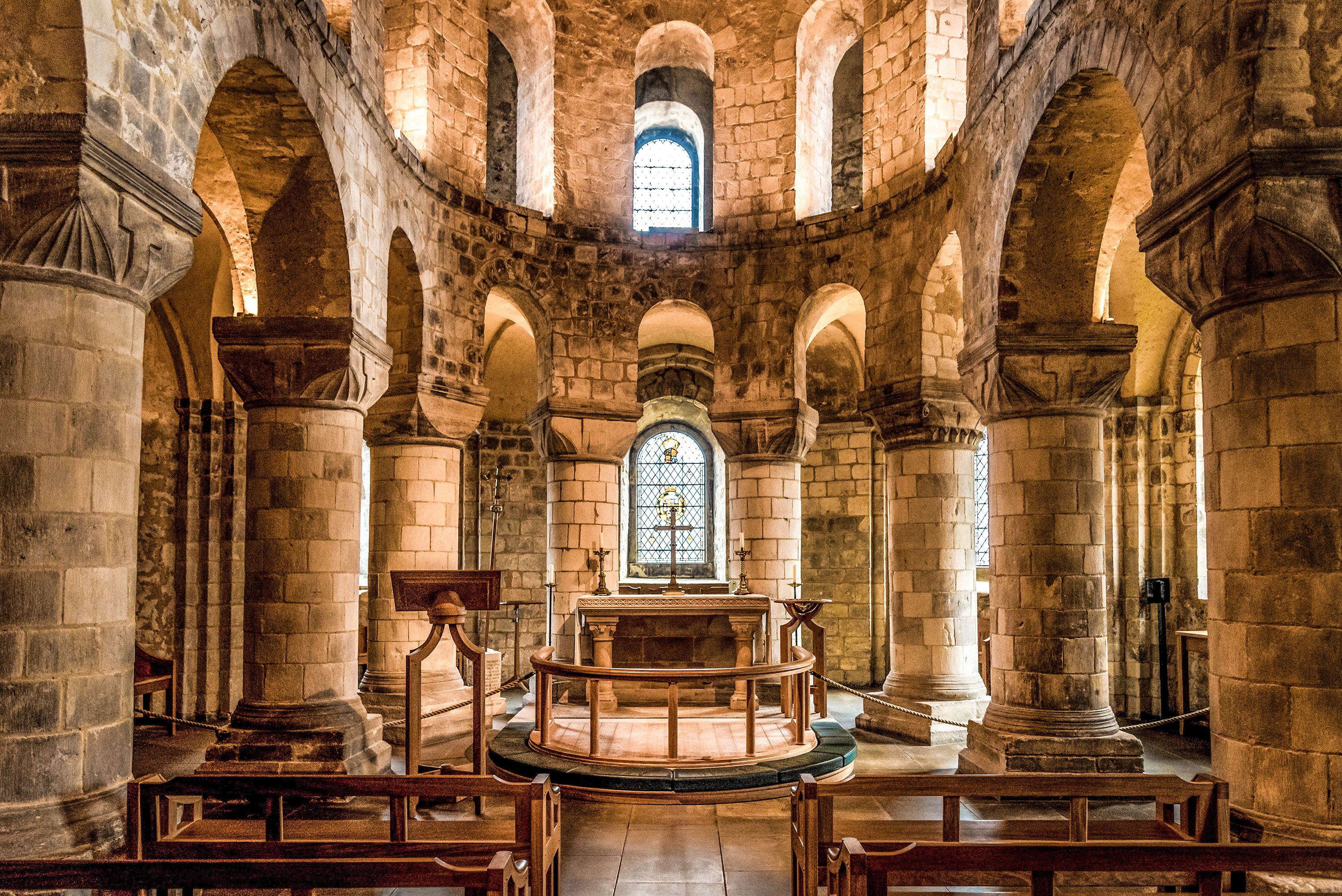 Interior of stone chapel with wooden pews and windows.