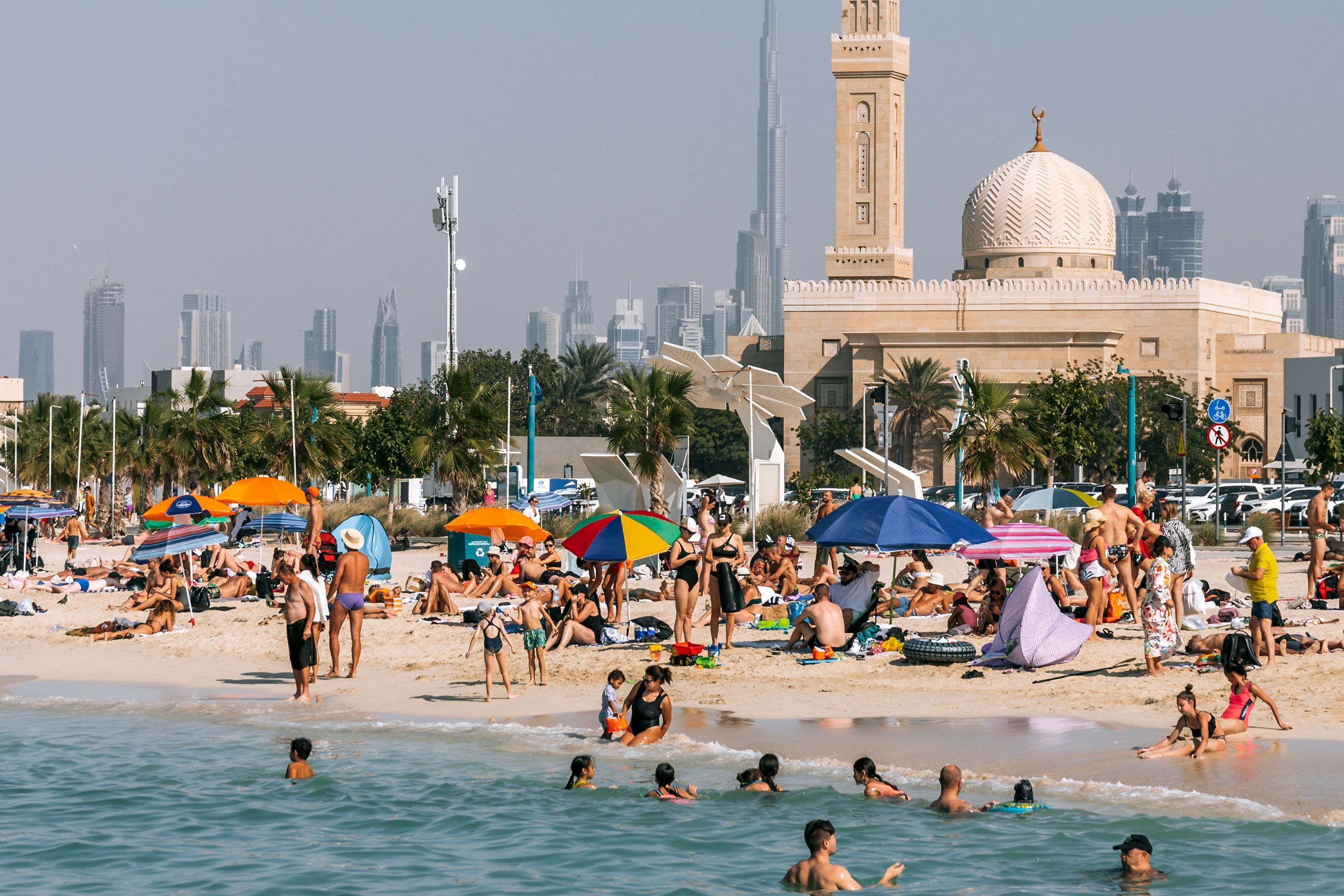 Crowds relax and take part in beach activities on the sandy shore of Kite Beach in Dubai with the Burj Al Arab visible in the distance.