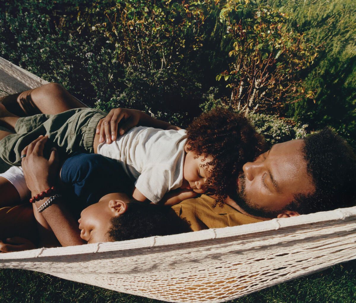 A man and two small children slumber in a garden hammock