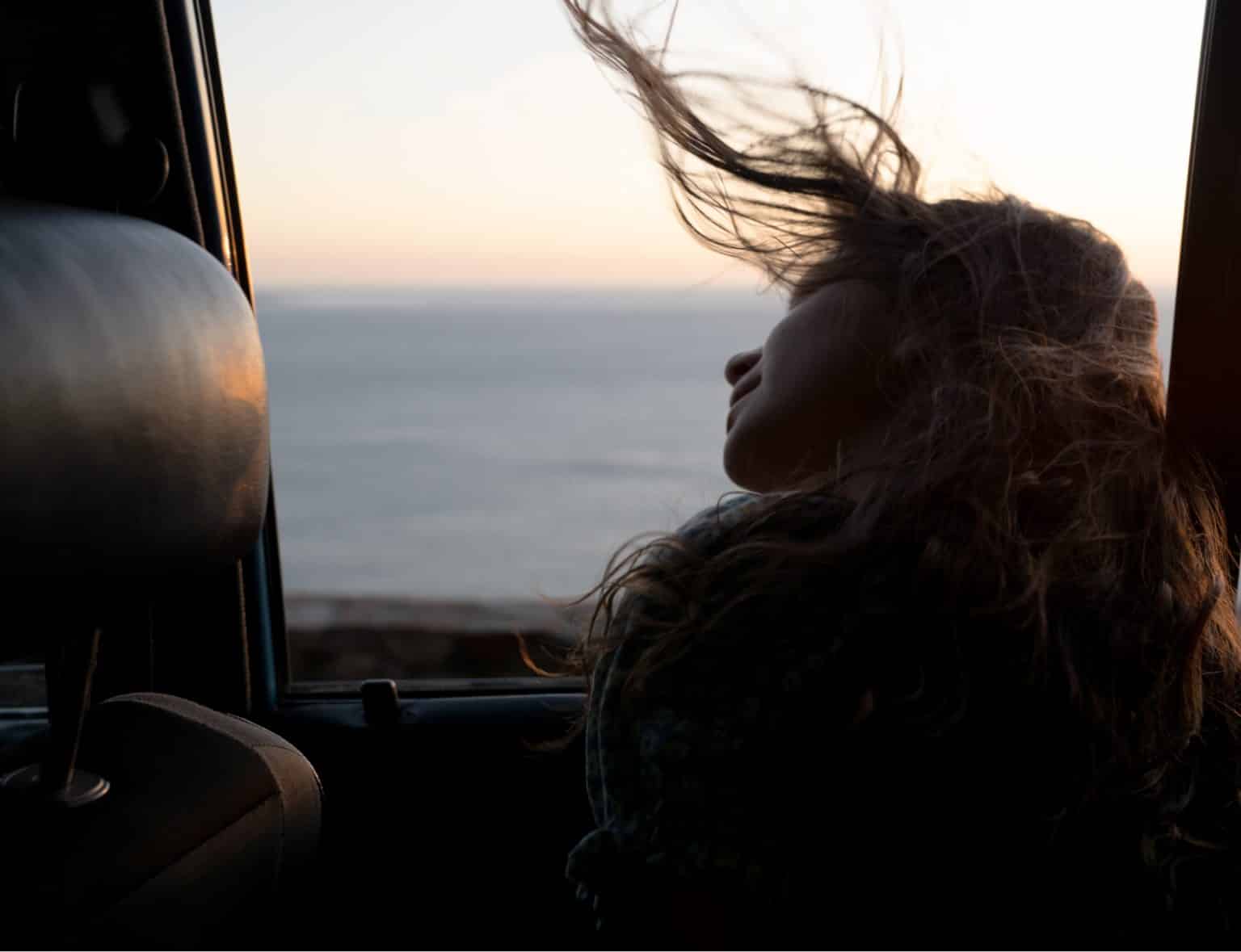 A woman leans out of an open car window, her long hair blowing in the wind