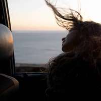 A woman leans out of an open car window, her long hair blowing in the wind