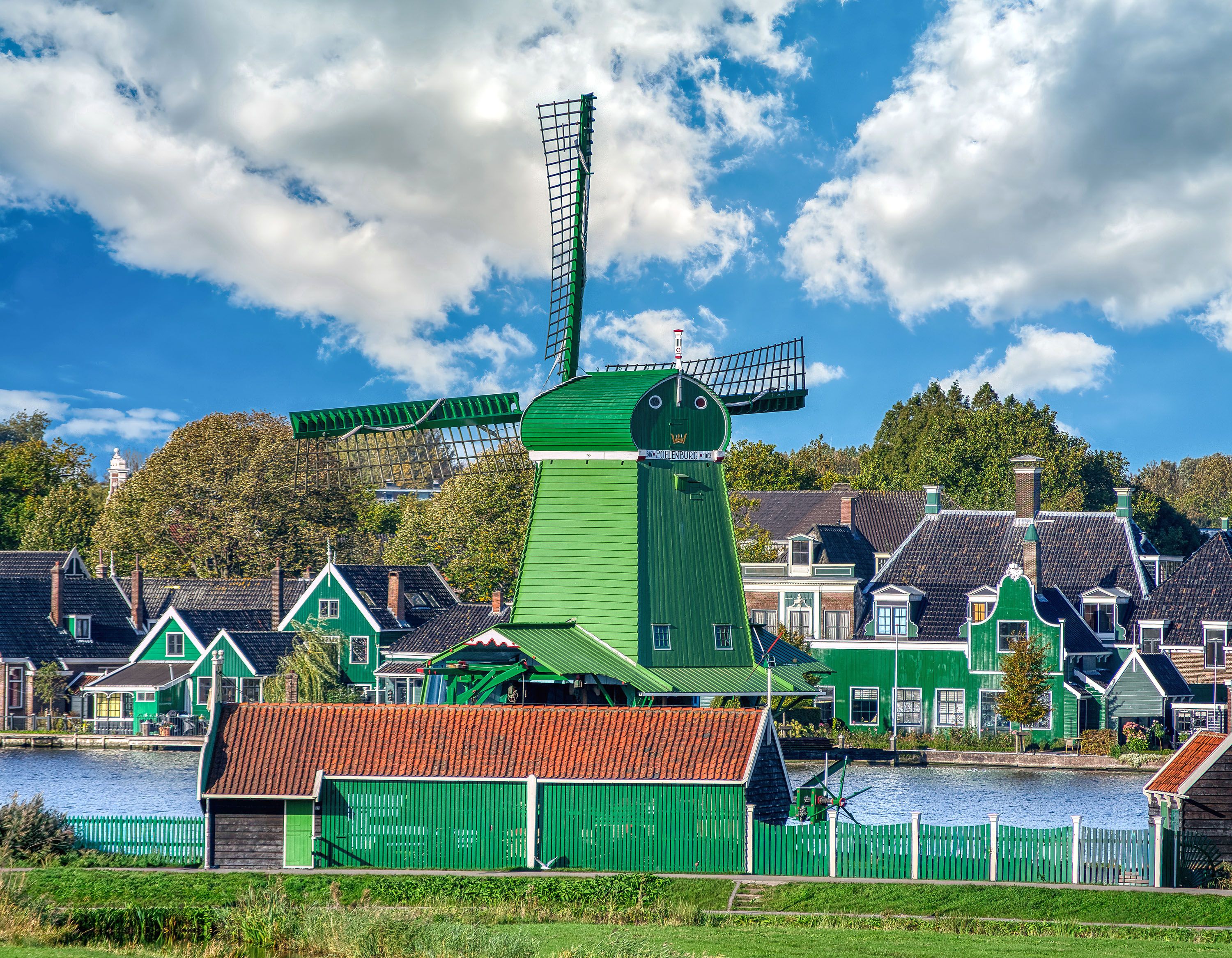 Green building and large green windmill with waterfront homes, blue sky and puffy clouds.