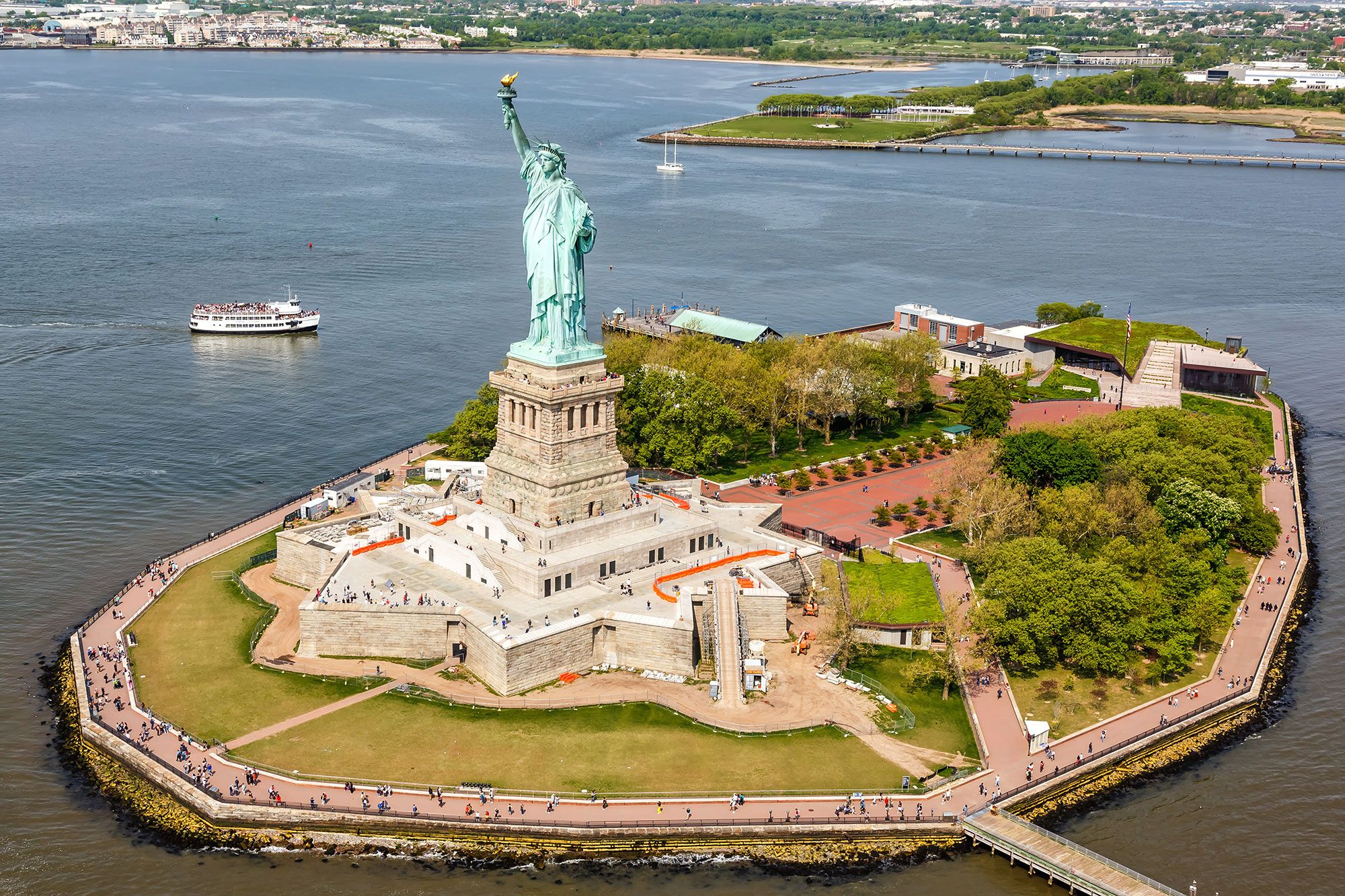 Aerial view of a statue of a green woman holding a gold torch in the air on an island.