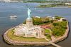 Aerial view of a statue of a green woman holding a gold torch in the air on an island.