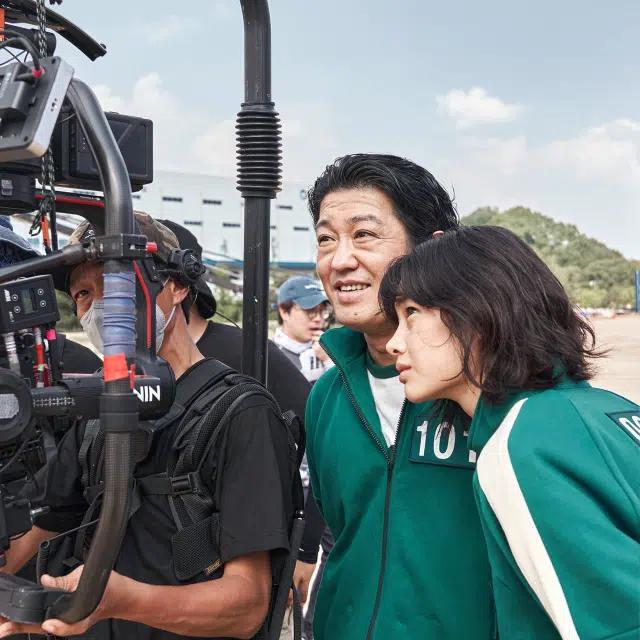 Two stars of Squid Game look at a camera in a behind the scenes moment