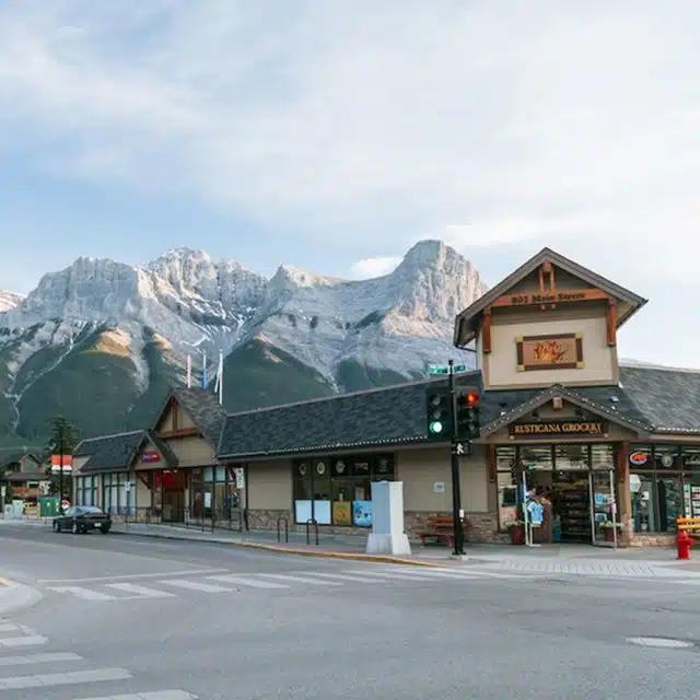 A grocery store at a crossroads backed by the snow-capped Rocky Mountains in the distance in Canmore, Canada