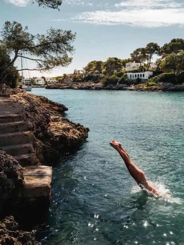 A person diving off stone steps into a bay in Mallorca