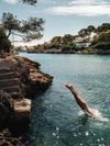 A person diving off stone steps into a bay in Mallorca