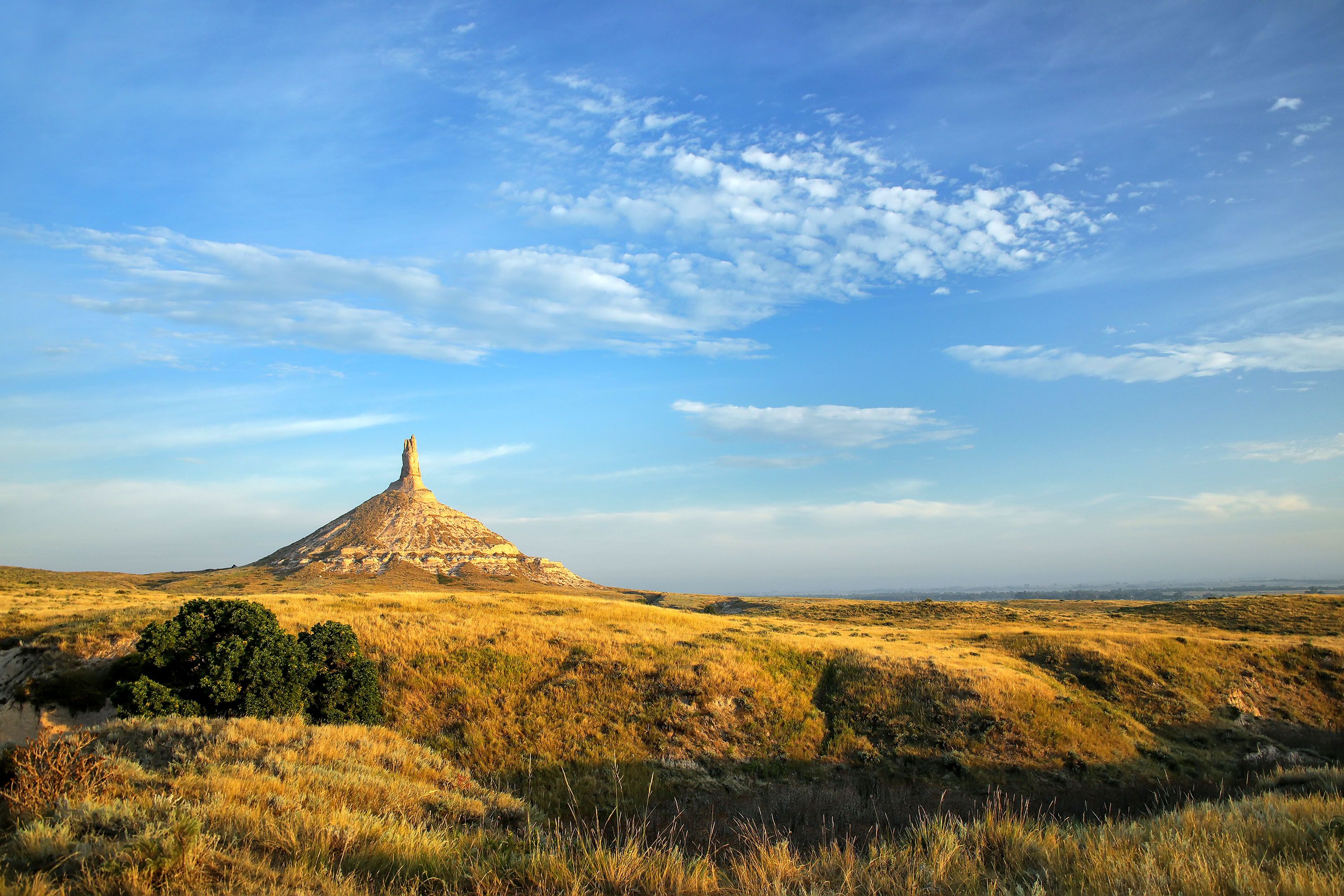 A chimney-shaped hill sitting as the highest point on a grass plain.