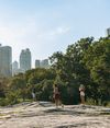 People stand atop the rocks in Central Park with the Manhattan skyline in the distance in New York City