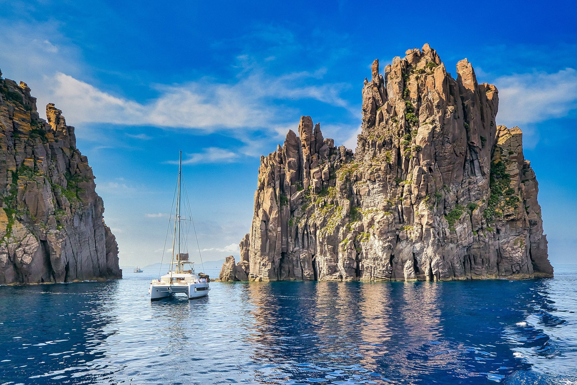 A boat sitting in the water close to the cliffs of Basiluzzo Island in Italy.