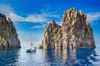 A boat sitting in the water close to the cliffs of Basiluzzo Island in Italy.