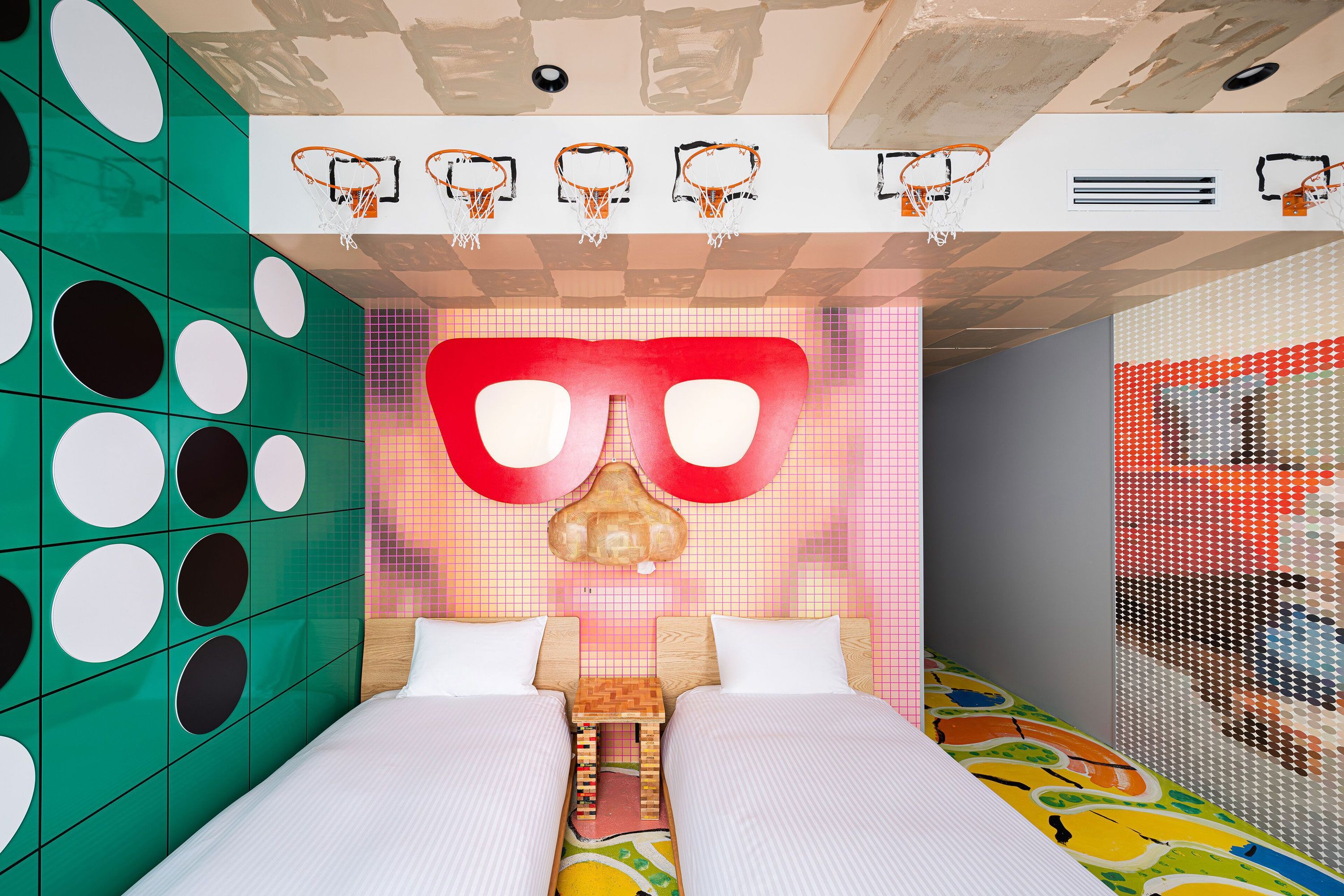 A small room with a bed in the foreground and different colored wall behind with a small desk and chair sitting by a window.