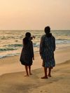 A woman and young girl stand on the sand of Fort Kochi beach in Kerala, India, as the girl points out to sea