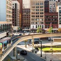 A trainline running over a road in Detriot, with skyscrapers in the background