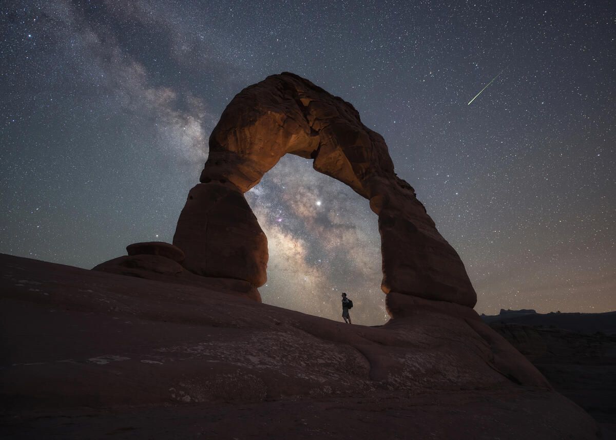 Delicate Arch in Arches National Park, with a hiker and starry sky seen beyond
