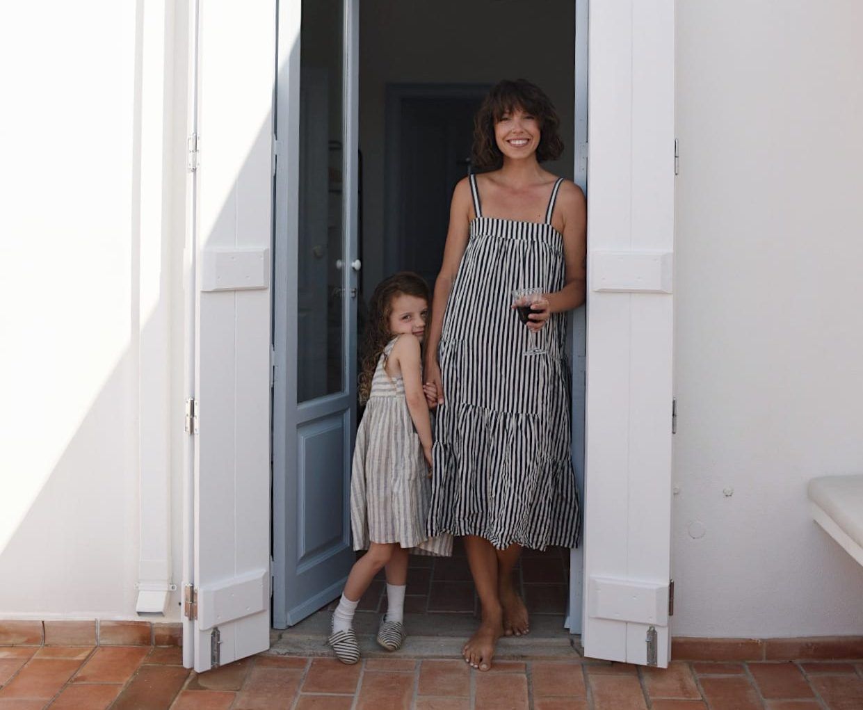Artist Meghan Bustard with her daughter in a doorway, both wearing striped sundresses
