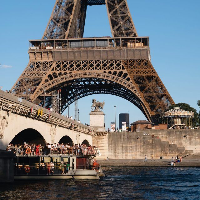 A Bateaux Mouches boat emerges from under a bridge as part of its trip down the Seine, Paris, passing the base of the Eiffel Tower 